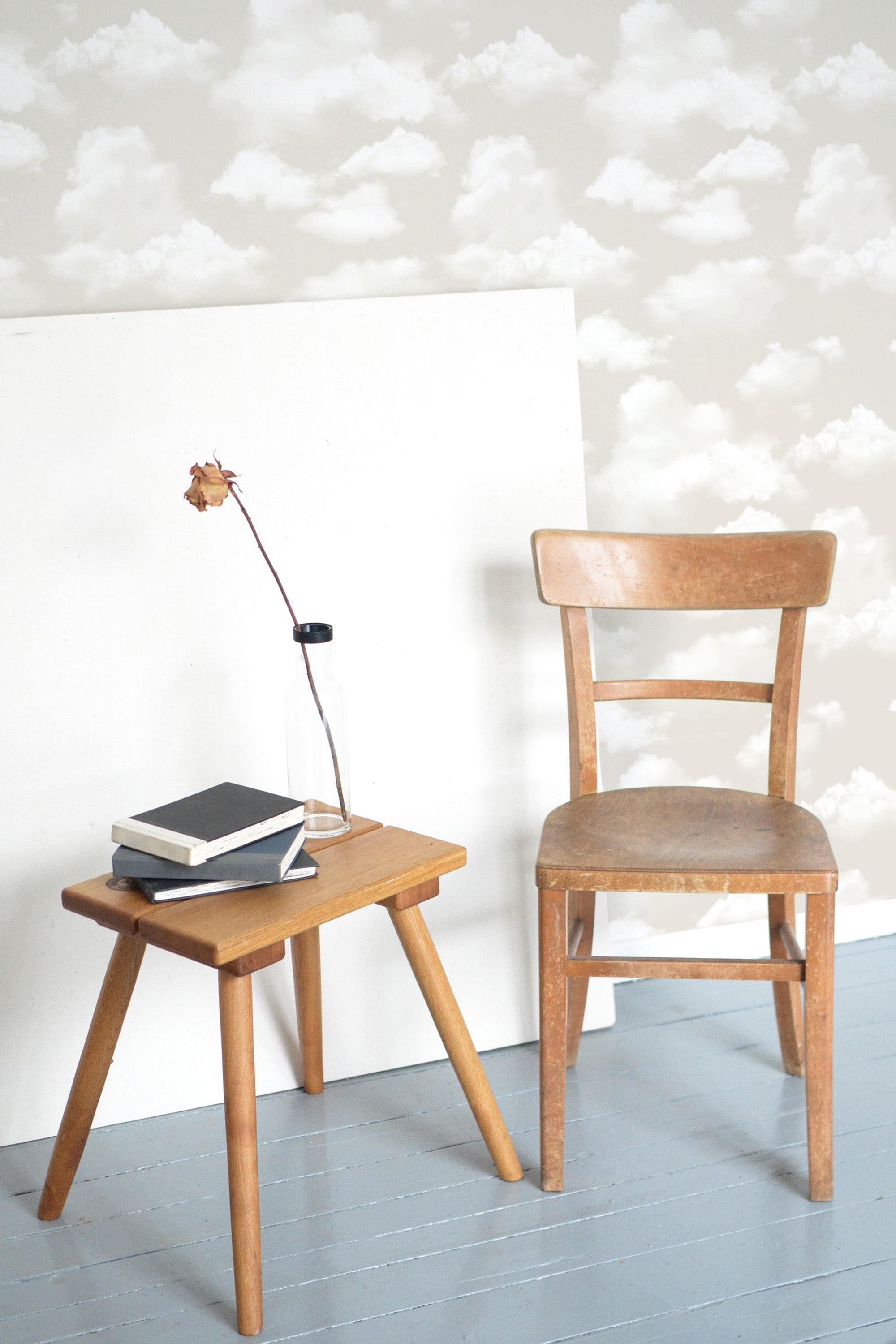 Self-adhesive wallpaper with a beachy clouds pattern in neutral tones on a room wall, complemented by a wooden chair and side table with books and a flower.