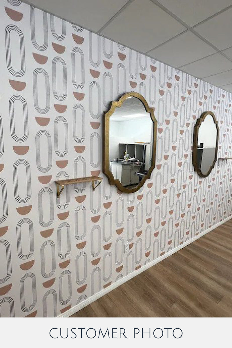 Boho circles wallpaper with a repeating pattern of ovals and semicircles in light pink and gray tones, installed on a wall with two mirrors. Traditional wallpaper.